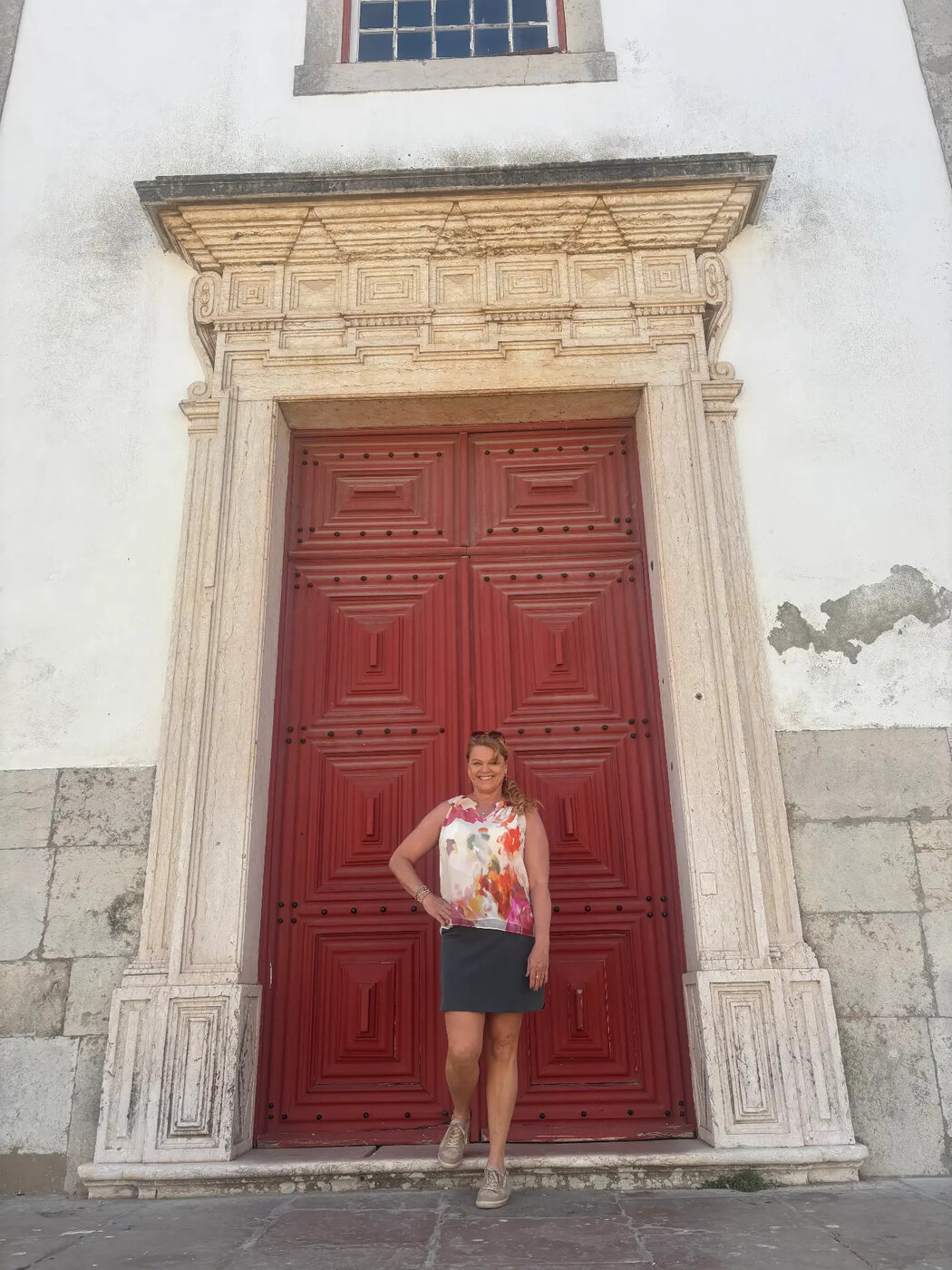 Sheila Chonis standing at the tall red doors of a historic church in Portugal
