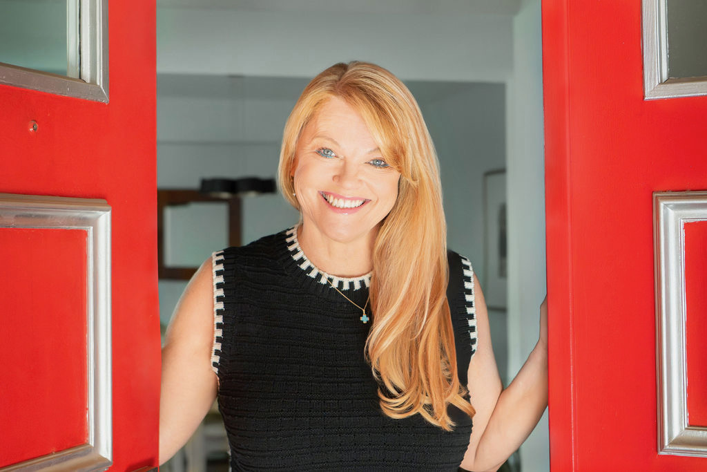 Sheila Chonis standing in an open red doorway, welcoming a client